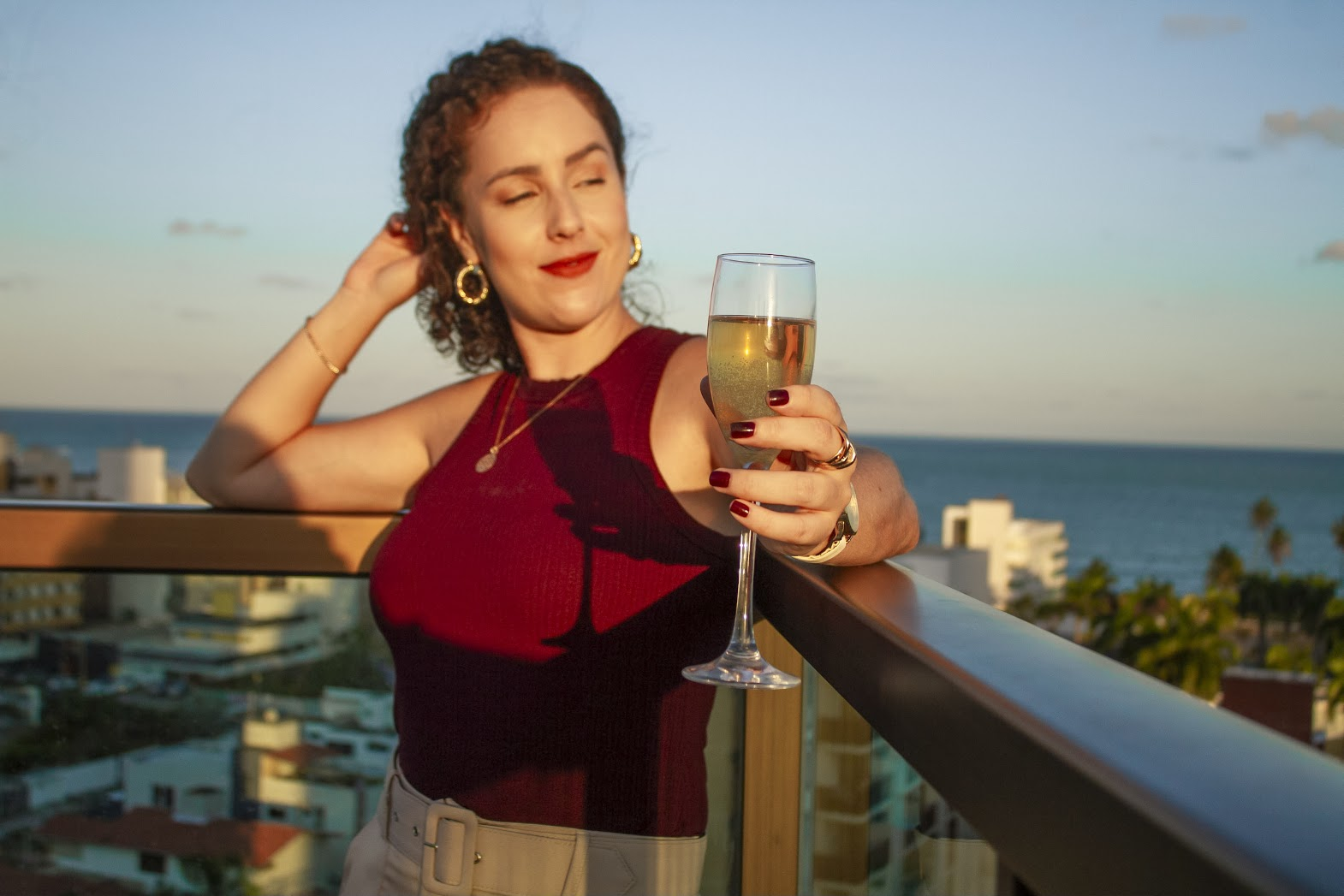 Thais Pavan em uma varanda com taça e vista para o mar
